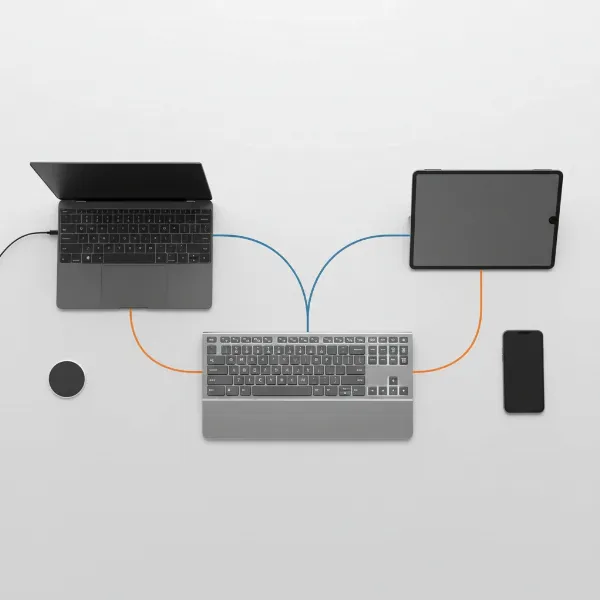 Sleek wireless keyboard seamlessly connecting to multiple high-end electronic devices via Bluetooth and a 2.4 GHz dongle on a modern desk.